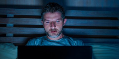 Man ligt in bed en kijkt op zijn laptop