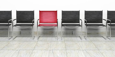 Rij lege zwarte stoelen met 1 rode stoel ertussen