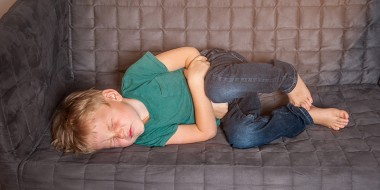 Kind ligt met buikkrampen op de bank