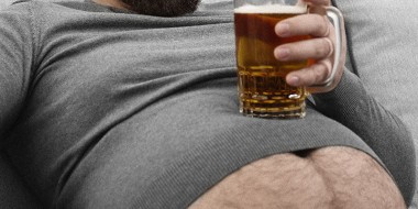 Man zit onderuitgezakt op de bank met een glas bier op zijn buik