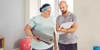 Vrouw met yogamat onder haar arm praat met man met een map in zijn hand.